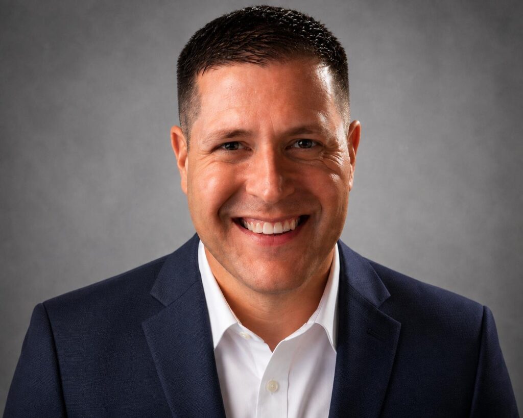 Scott Sanders, founder of Affordable Technology Solutions, in a blue blazer against a grey studio background